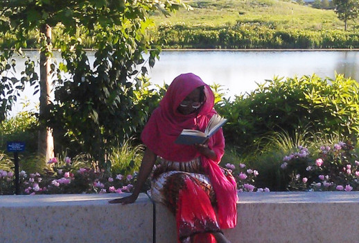 picture of Maryam Sharron Muhammad wearing a red dupatta and dress and sitting and reading by a lake in the Chicago Botanic Garden